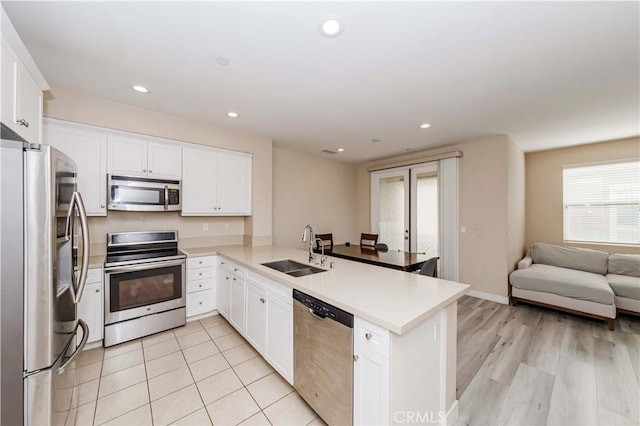 kitchen featuring kitchen peninsula, stainless steel appliances, a wealth of natural light, white cabinets, and sink