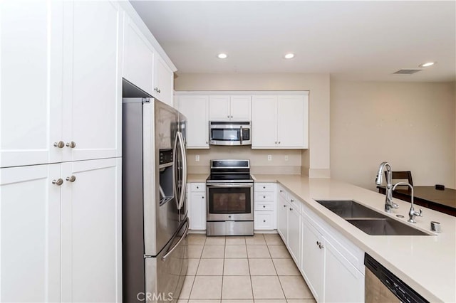 kitchen featuring kitchen peninsula, sink, light tile patterned floors, appliances with stainless steel finishes, and white cabinets