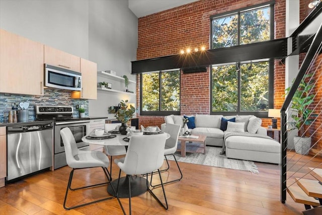 dining room featuring a towering ceiling, brick wall, and light hardwood / wood-style flooring