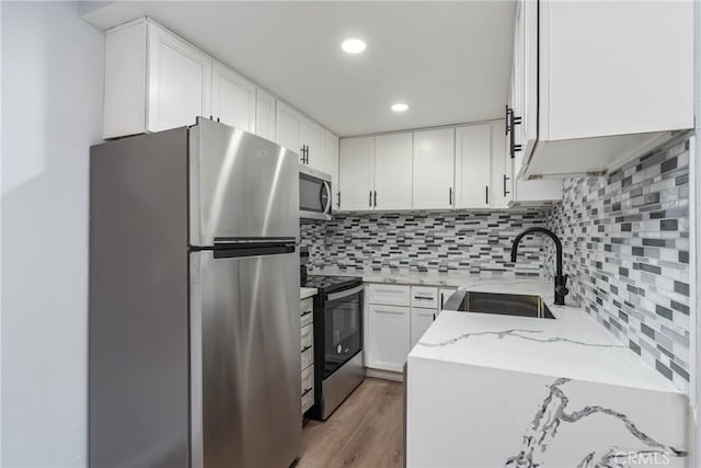 kitchen with appliances with stainless steel finishes, light stone countertops, sink, white cabinetry, and tasteful backsplash