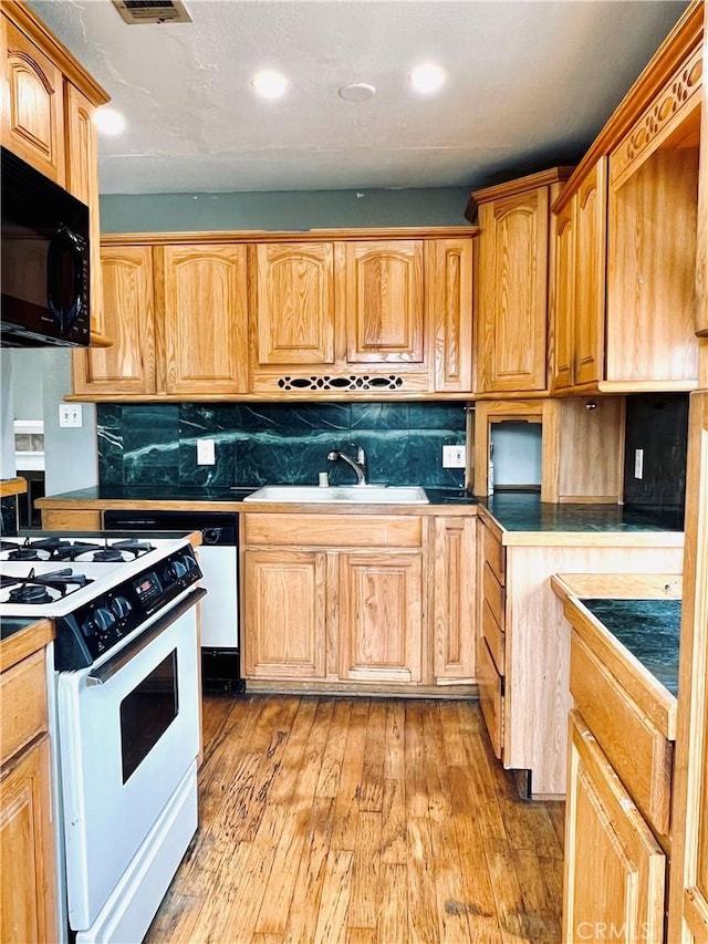 kitchen featuring black microwave, light wood-style flooring, gas range gas stove, decorative backsplash, and a sink