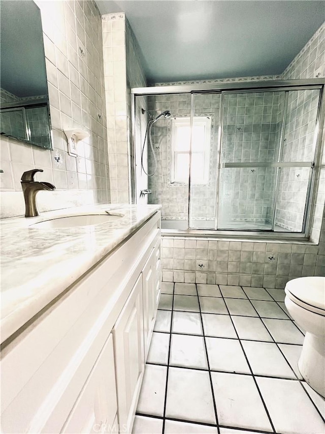 bathroom featuring toilet, tile patterned floors, vanity, and tile walls
