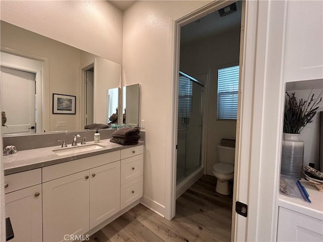 bathroom featuring toilet, wood-type flooring, vanity, and a shower with door