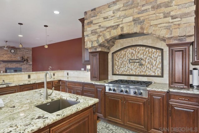 kitchen featuring stainless steel gas cooktop, sink, decorative light fixtures, backsplash, and light stone counters