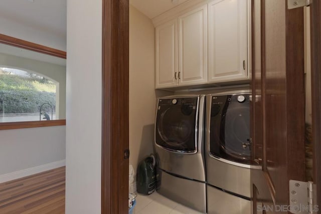 clothes washing area featuring separate washer and dryer, light hardwood / wood-style floors, and cabinets