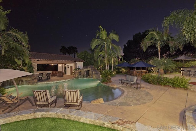 pool at night with exterior bar, an outbuilding, pool water feature, and a patio