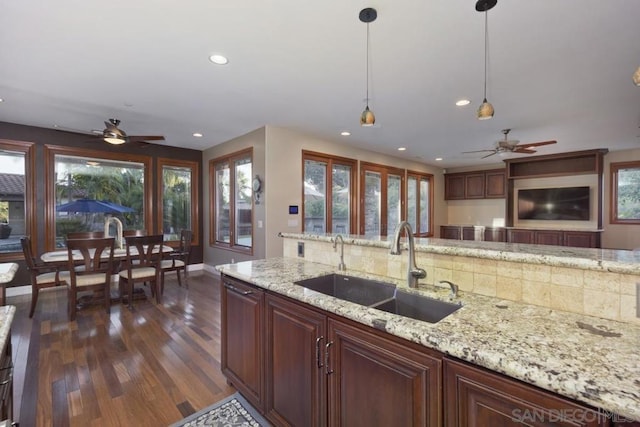 kitchen featuring decorative light fixtures, dark hardwood / wood-style flooring, ceiling fan, sink, and light stone counters