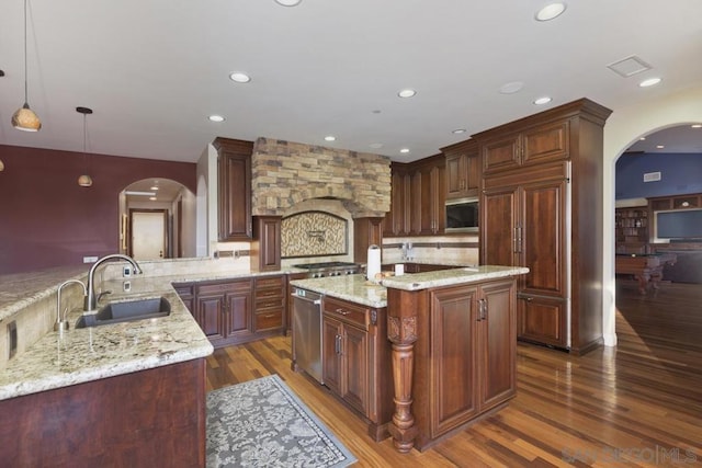 kitchen featuring hanging light fixtures, appliances with stainless steel finishes, sink, light stone countertops, and an island with sink