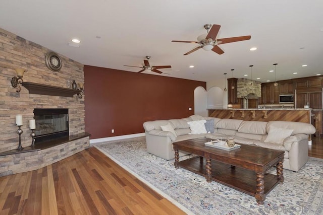 living room with ceiling fan, a stone fireplace, and light hardwood / wood-style floors