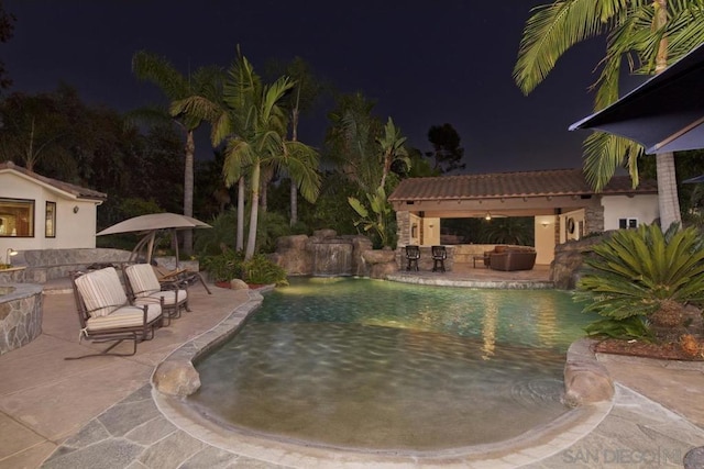 pool at twilight with a patio area, an outdoor hangout area, and an outdoor structure