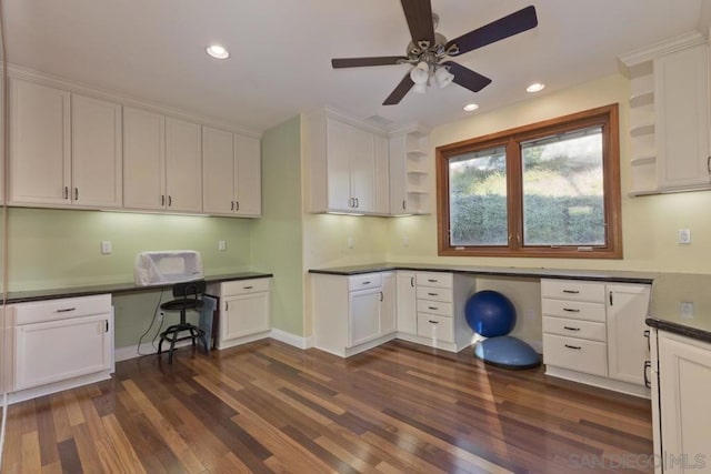 unfurnished office with ceiling fan, built in desk, and dark hardwood / wood-style flooring