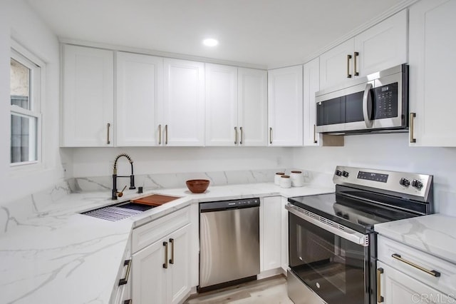 kitchen featuring stainless steel appliances, white cabinetry, light stone counters, and sink