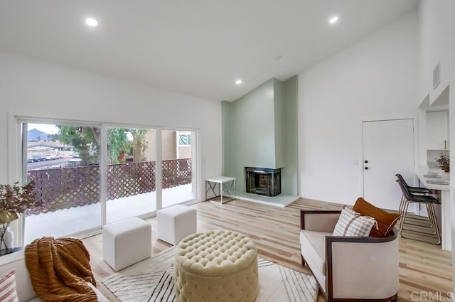 living room featuring a wood stove, light hardwood / wood-style floors, and high vaulted ceiling