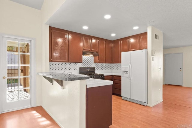 kitchen featuring gas stove, white refrigerator with ice dispenser, light hardwood / wood-style floors, kitchen peninsula, and a breakfast bar area