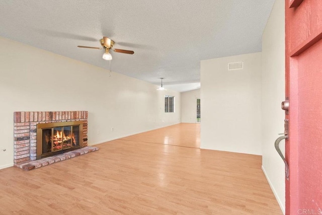 unfurnished living room with a textured ceiling, lofted ceiling, light hardwood / wood-style floors, ceiling fan, and a brick fireplace