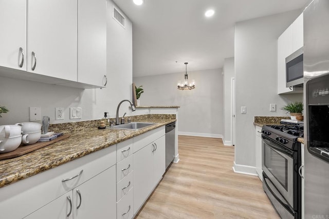 kitchen with an inviting chandelier, appliances with stainless steel finishes, hanging light fixtures, white cabinets, and sink