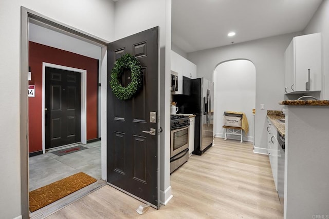 kitchen with baseboards, white cabinets, arched walkways, stainless steel appliances, and light wood-type flooring