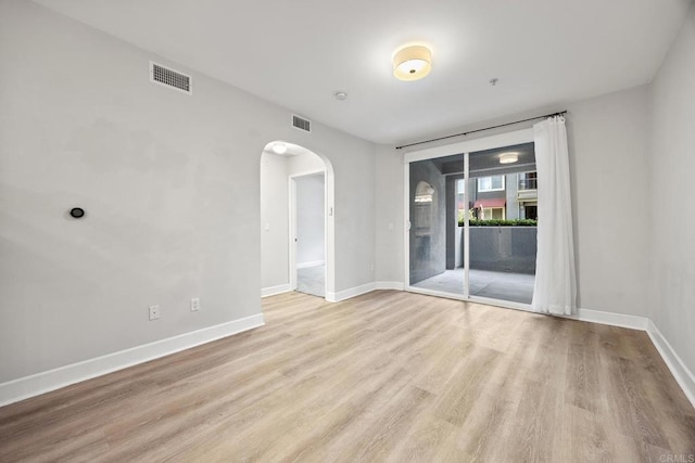 empty room featuring light wood-style floors, arched walkways, visible vents, and baseboards