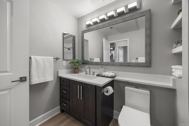 bathroom featuring toilet, baseboards, wood finished floors, and vanity