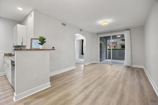 spare room with light wood-type flooring, arched walkways, visible vents, and baseboards