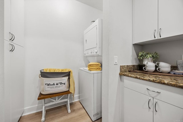 laundry area with light wood finished floors, baseboards, and stacked washer / dryer