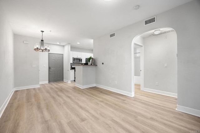 unfurnished living room with arched walkways, light wood finished floors, visible vents, and baseboards