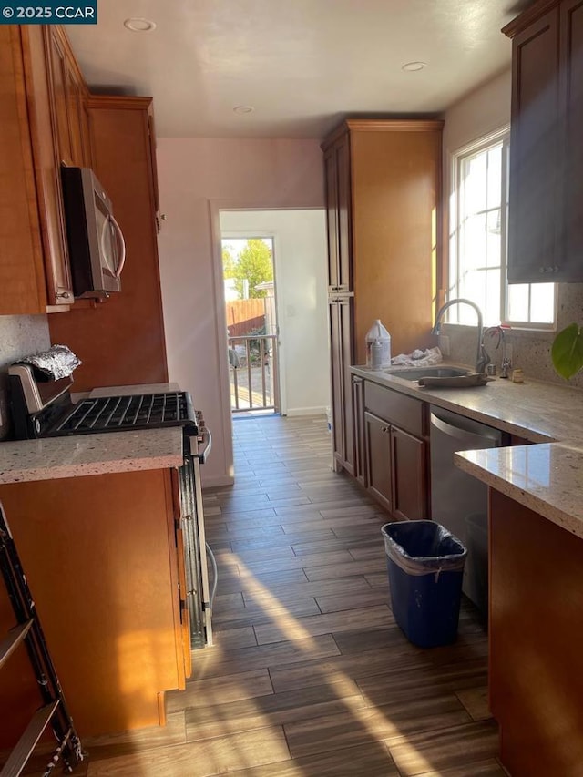 kitchen with light wood-type flooring, sink, light stone counters, and stainless steel appliances