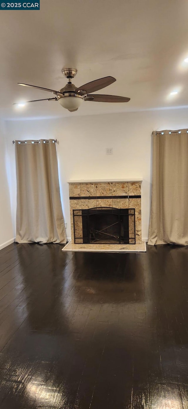 unfurnished living room featuring a tiled fireplace, wood-type flooring, and ceiling fan