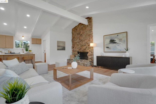 living room featuring light hardwood / wood-style floors, vaulted ceiling with beams, a stone fireplace, and sink