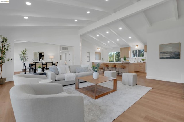 living room with light wood-type flooring, vaulted ceiling with beams, and sink