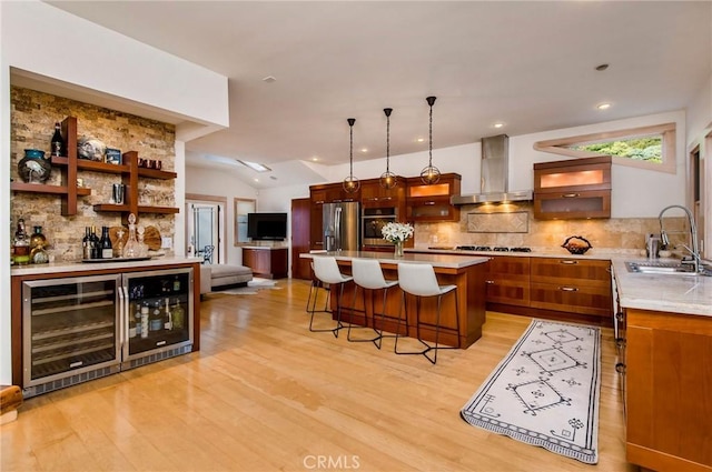 kitchen featuring pendant lighting, wall chimney range hood, stainless steel appliances, decorative backsplash, and sink