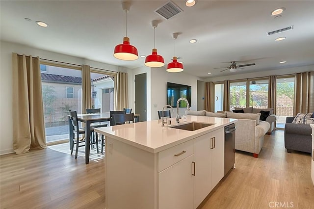 kitchen featuring decorative light fixtures, ceiling fan, sink, white cabinetry, and an island with sink