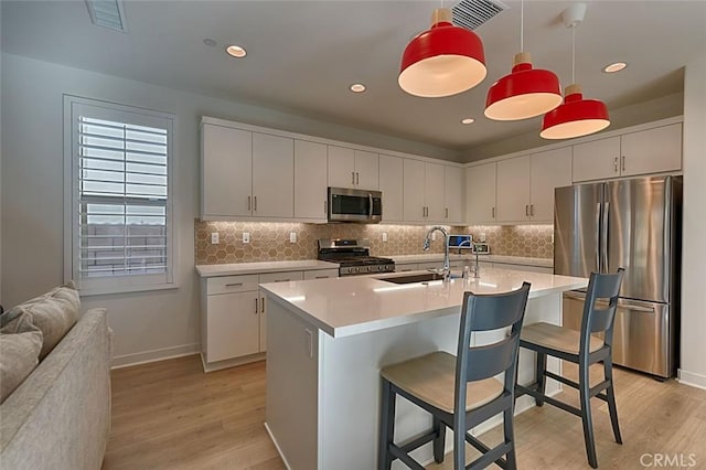 kitchen with a kitchen bar, sink, a kitchen island with sink, stainless steel appliances, and white cabinets