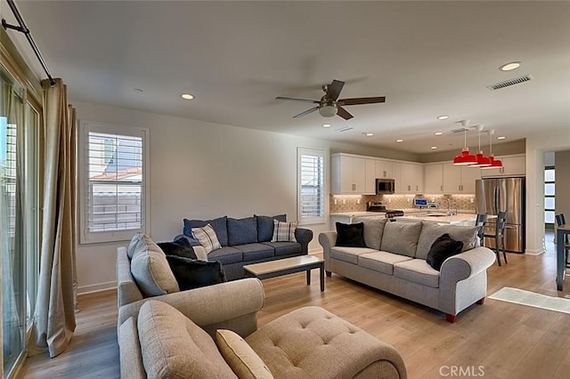 living room featuring ceiling fan, light wood-type flooring, and sink