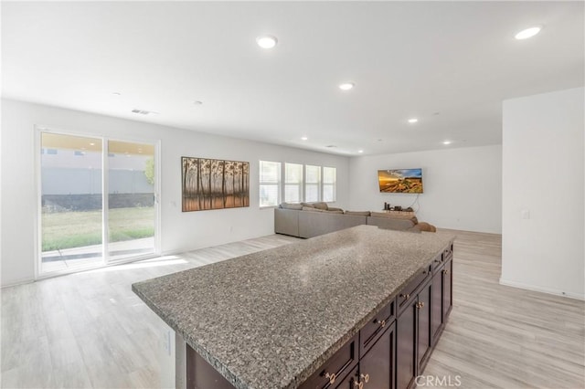 kitchen with light hardwood / wood-style floors, light stone countertops, a center island, and dark brown cabinets