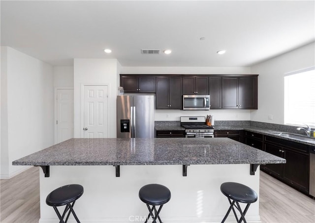 kitchen featuring a kitchen island, stainless steel appliances, dark stone countertops, sink, and a breakfast bar