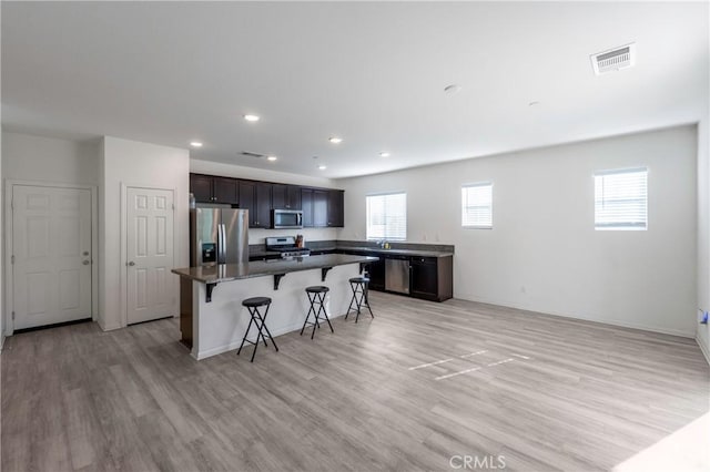 kitchen with appliances with stainless steel finishes, a kitchen island, a kitchen breakfast bar, light wood-type flooring, and dark brown cabinets