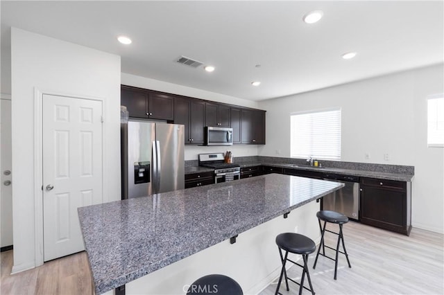 kitchen featuring appliances with stainless steel finishes, a center island, dark stone countertops, a kitchen breakfast bar, and sink