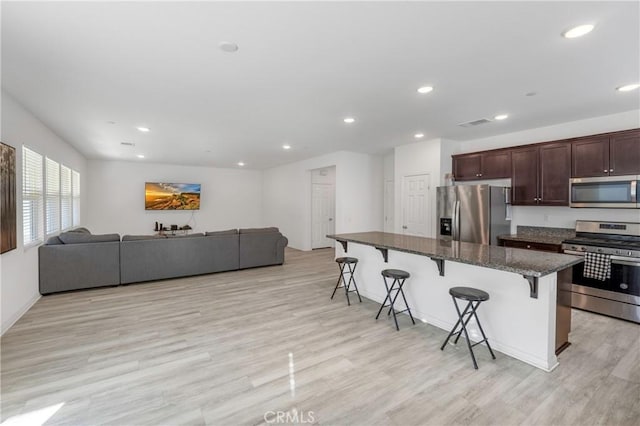 kitchen featuring a kitchen bar, stainless steel appliances, dark stone counters, a kitchen island, and dark brown cabinetry