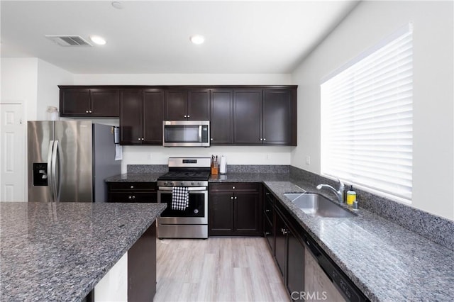 kitchen with sink, dark stone countertops, stainless steel appliances, and light hardwood / wood-style flooring