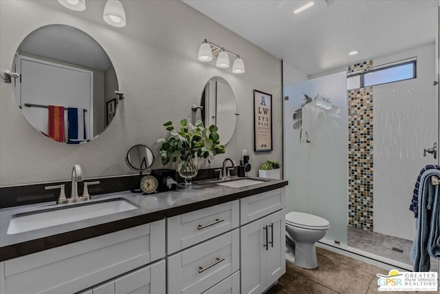 bathroom featuring toilet, vanity, tile patterned floors, a textured ceiling, and a tile shower