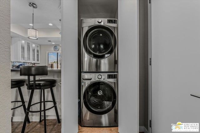 clothes washing area with hardwood / wood-style floors and stacked washer and dryer