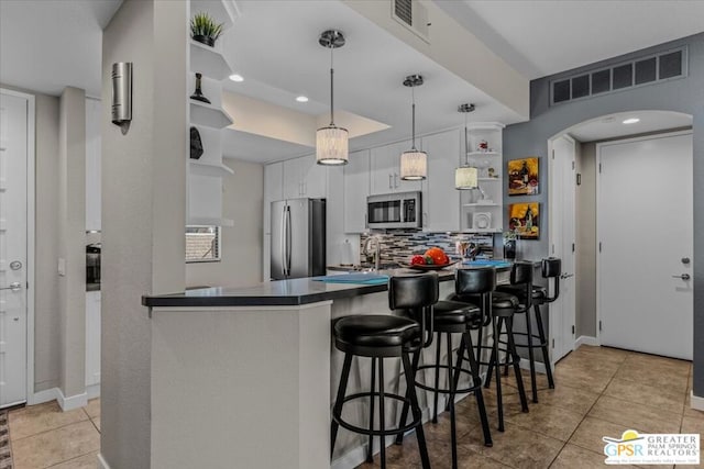 kitchen with pendant lighting, appliances with stainless steel finishes, white cabinetry, backsplash, and kitchen peninsula