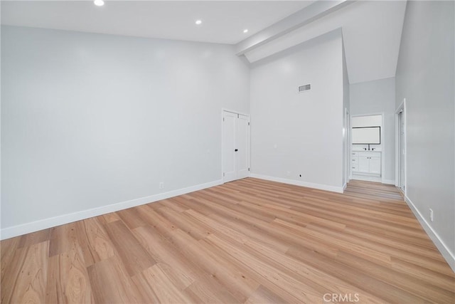 spare room with light wood-type flooring and high vaulted ceiling