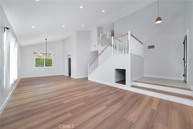 unfurnished living room with high vaulted ceiling, an inviting chandelier, and light hardwood / wood-style floors