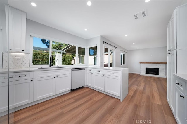 kitchen with white cabinetry, a brick fireplace, stainless steel dishwasher, light hardwood / wood-style flooring, and sink