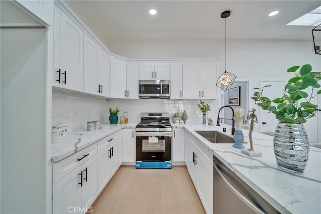 kitchen featuring a skylight, stainless steel appliances, light stone countertops, pendant lighting, and white cabinets