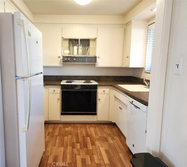 kitchen featuring white appliances, dark countertops, a sink, and white cabinets