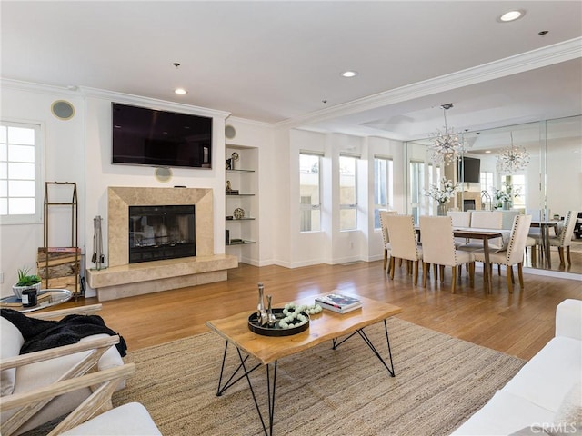 living room with a notable chandelier, light hardwood / wood-style floors, ornamental molding, built in shelves, and a high end fireplace