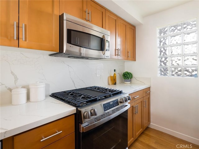 kitchen with stainless steel appliances, light hardwood / wood-style flooring, backsplash, and light stone countertops